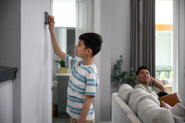 istock Father watches as young boy adjust temperature control on thermostat smart home automation 2156180611