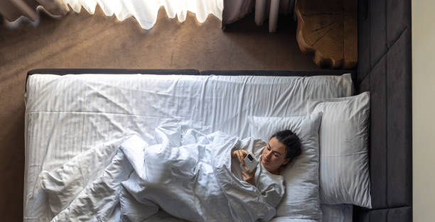 istock Young woman lying in bed and using a smartphone, top view. 2156183116