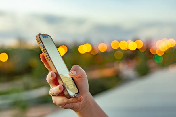 Young woman's hand holding and using her iPhone against a twilight urban background.