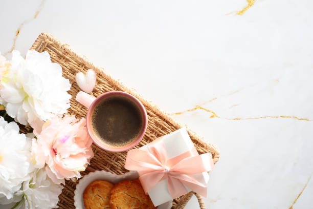 istock Wicker tray with peonies, coffee cup, cookies, gift box on marble surface. Cozy morning breakfast. Flat lay, top view. 2156184908