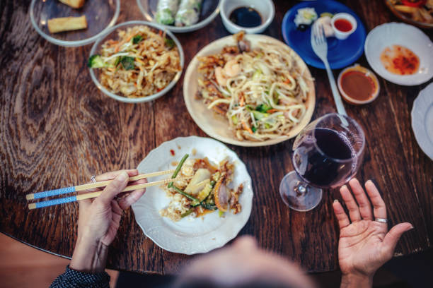 overhead view on female hands holding chopsticks with asian food on lunch table