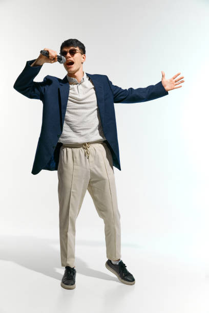 artistic man, vocalist dressed casual attire with sunglasses performing, singing with microphone against white studio background. Concept of music, festivals, contemporary art, hobby, creativity. Ad