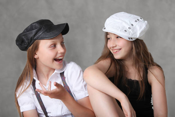 two cute stylish preteen girls chatting on grey background