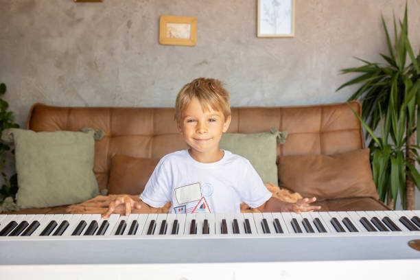 Child, blond boy, playing piano at home, learning