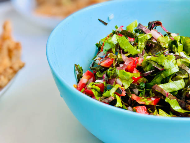 istock Fresh Green Salad in Blue Bowl with Meat Dish in Background 2156202042