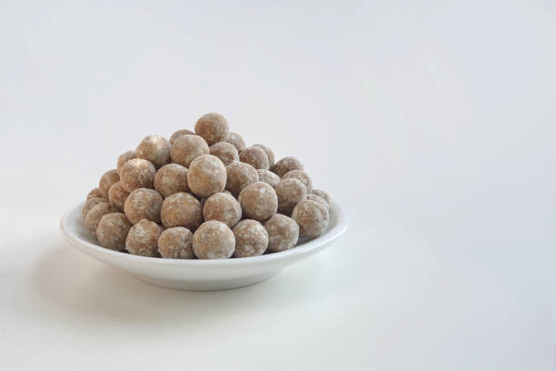 Close-up of golden, round Indian sweet treats (ladoo) placed inside a clear plastic jar, with a blurred and colorful shop background. The image evokes a warm, festive, and traditional Indian atmosphere.