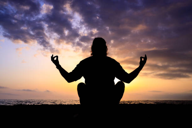 A man is sitting on the beach, meditating in the sunset