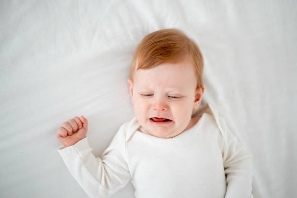 crying baby boy with red hair in a white bodysuit on the bed, top view, Lifestyle, baby of six months lies on the back and cries for his mother crying baby boy with red hair in a white bodysuit on the bed, top view, Lifestyle, baby of six months lies on the back and cries for his mother. half dozen babies stock pictures, royalty-free photos & images