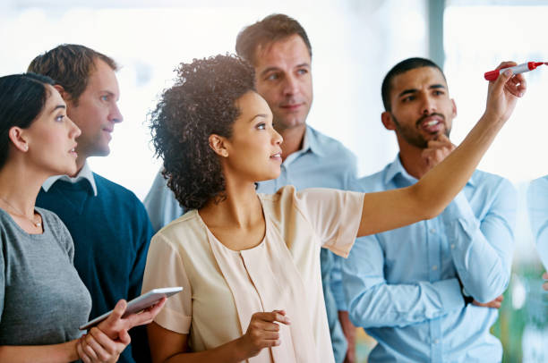 istock Business people, writing and coaching with glass board for schedule planning, tasks or agenda at office. Group of young and creative employees taking notes for discussion, brainstorming or startup 2156216508