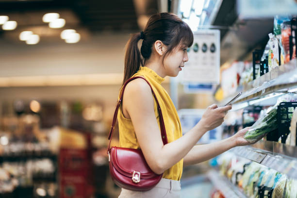 An Asian woman perusing the shelves stocked with an array of fresh produce, pantry staples, and household items. With a focused expression, she selects items from her shopping list, occasionally pausing to compare prices or inspect the quality of products an asian woman perusing the shelves stocked with an array of fresh produce, pantry staples, and household items. with a focused expression, she selects items from her shopping list, occasionally pausing to compare prices or inspect the quality of products