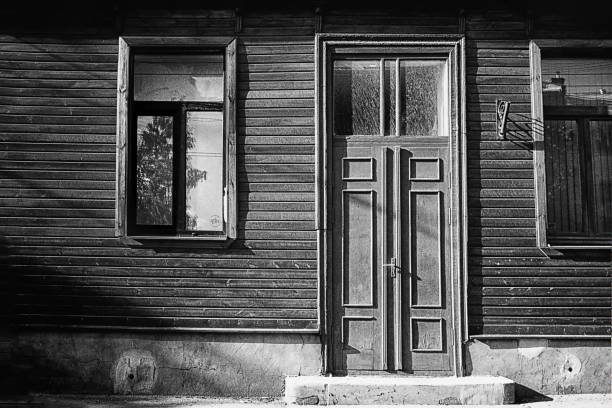 A door of carved wood of a residential building/home in a narrow alley/street with residential buildings in the medieval village of Olympi (or Olimpi or Olympoi or in Greek: Ολύμποι) on the Greek Island of Chios in the Aegean Sea. The image was captured on grainy (ISO 400) black and white analogue film by a 35 mm old-fashioned film camera. Olympi is part of a group of villages on Chios called the mastic villages (including Mesta, Pyrgi, Armolia, Vessa, and other villages) because they produced and traded mastic gum from mastic trees. These villages have been added in the List of the Intangible Cultural Heritage of Humanity of UNESCO. The houses of the mastic villages are build side-by-side to each-other originally forming the outer wall of a castle with only one (as in Olympi) or just a few entrances that were closed by gates at night, and when pirates approached the village. The streets are very narrow, and most of them are covered with arches and vaults. The streets form a maze to slow down any enemy that managed to enter the gates and ease the defence of the most important buildings located in the center of the village. The image is part of a series of black and white analogue photographs of picturesque Greek Island Villages on the Island of Chios.