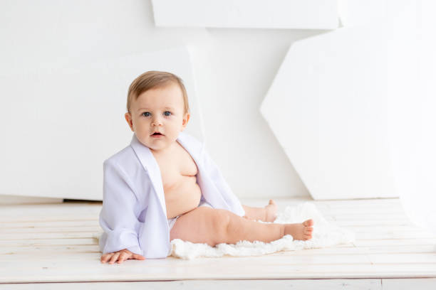 istock a small fat baby six months old in a white jacket and diapers sits on a light background, space for text 2156221214