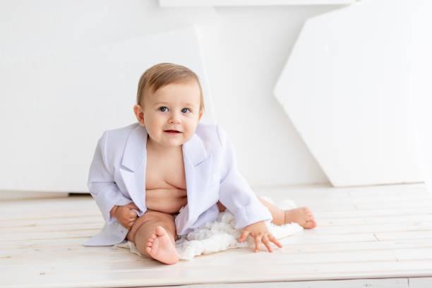 istock a small fat baby six months old in a white jacket and diapers sits on a light background, space for text 2156221218