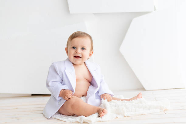 istock a small fat baby six months old in a white jacket and diapers sits on a light background, space for text 2156221224