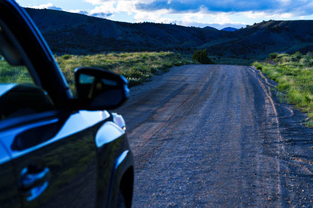Backcountry Road Ahead with Blurred SUV Vehicle in Foreground - Dirt road leading off into the mountains with selective focus on middle ground area and blurred vehicle in foreground and nobody else around in scenic backcountry area.