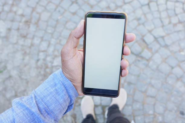 istock Person in blue shirt holds smartphone with blank screen, outdoors on cobblestone background 2156225054