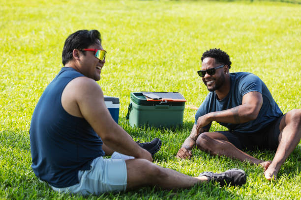 istock Two multiracial men sitting on grass, laughing 2156229590