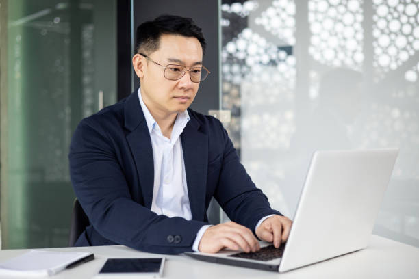 istock Asian mature man working on laptop computer in modern office setting 2156232926