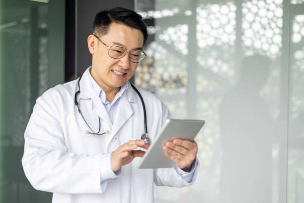 istock Smiling Asian doctor using a tablet in modern hospital setting 2156238356