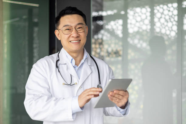 istock Asian mature male doctor using tablet and smiling in a modern hospital setting 2156238638