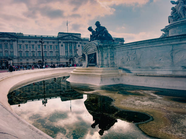 majestic Buckingham Palace as seen from behind a fountain. The reflection in the water adds a captivating element, highlighting the grandeur of one of London's most iconic landmarks. Perfect for those looking to capture the essence of British royalty and elegance.