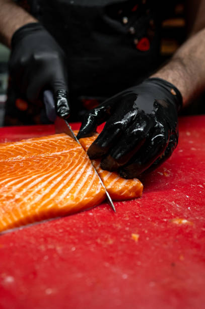 istock Hands in black gloves expertly slice fresh salmon on a vibrant red cutting board 2156244043