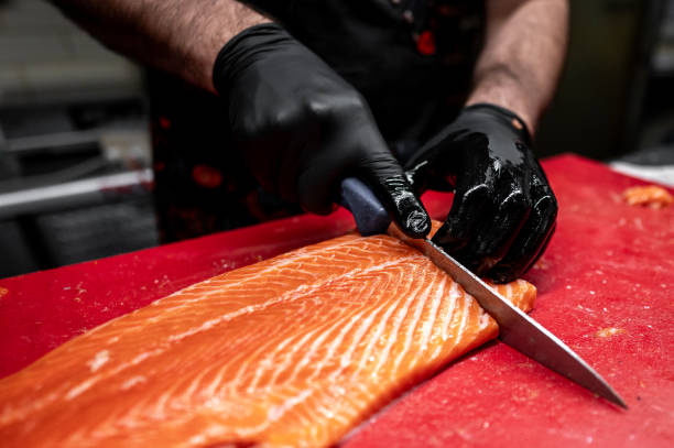 istock Hands in black gloves expertly slice fresh salmon on a vibrant red cutting board 2156244086