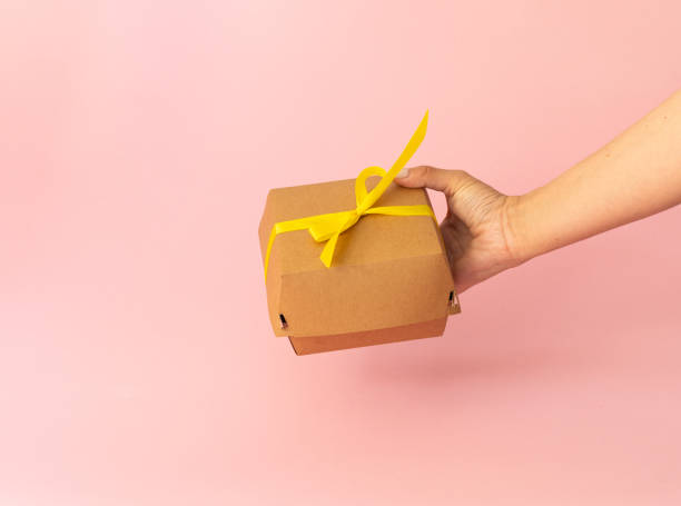istock cardboard packaging in female hand, bento cake on light pink background, yellow bow 2156244182