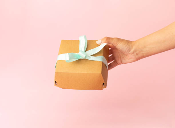 istock cardboard packaging in female hand, bento cake on light pink background, light blue bow 2156244202