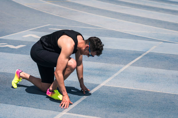 istock A man is crouched on a track, preparing to run. He is wearing sunglasses and spiked running shoes. 2156247282