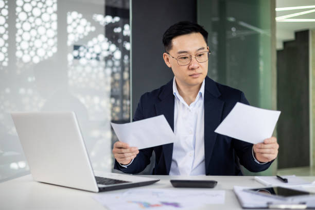 istock Asian mature man working at modern office, reviewing documents with focus and concentration 2156247444