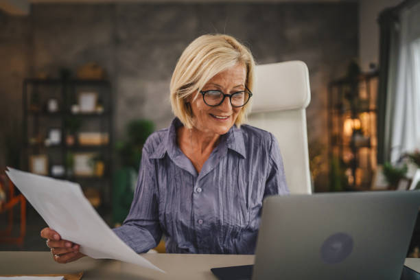 istock Mature senior woman work from home use laptop and hold documents 2156254832
