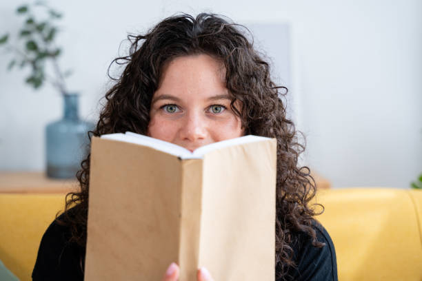 istock Young lady is smiling while holding a book in front of her face 2156255364