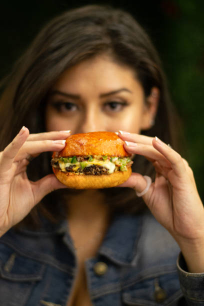 istock Woman holding a hamburger with her eyes in the background. 2156257016