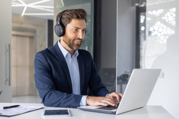 istock Smiling businessman with headphones using laptop in office 2156257186