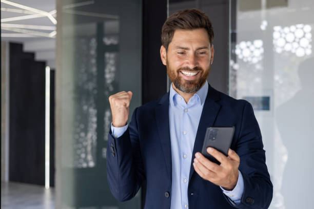 istock Successful businessman celebrating with smartphone in office 2156258434