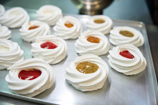 Close-up of fruit pavlova topped with whipped cream, strawberries, peaches, grapes, and blueberries on display at a bakery counter.