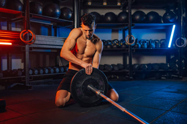 Muscular man covered in sweat adjusting weights on a bar during the weightlifting training in the gym health club. Handsome male lifting heavy weights in a gym. Copy space.