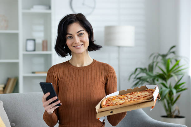 istock Woman enjoying fresh pizza while using smartphone in cozy home setting 2156262331