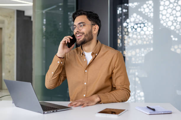 istock Smiling professional man on phone call at his office desk with laptop and tablet 2156263151