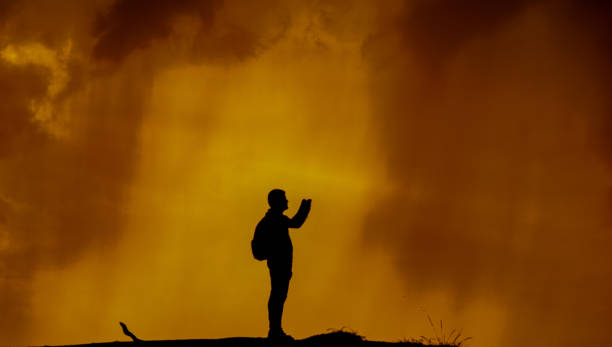 silhouette of a young hispanic latino man taking a picture with his mobile phone in the background at sunset
