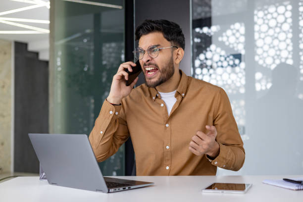 istock Frustrated businessman on phone call while sitting at desk in modern office 2156265909