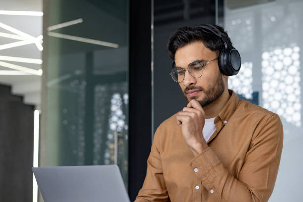 istock Young professional with headphones working on laptop in modern office setting 2156266802