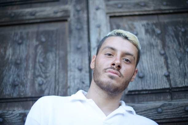 Portrait of a contemplative young man in a white shirt posing before an old rustic wooden door, looking offcamera