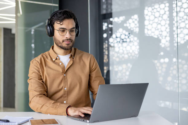 istock Focused man working on laptop wearing headphones in modern office 2156267045