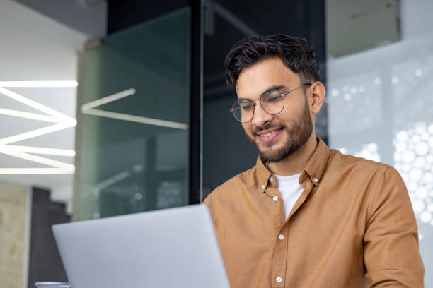 istock Smiling young man in a modern office working on a laptop 2156267713