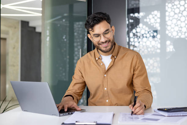 istock Smiling businessman working on laptop and taking notes in modern office 2156267755