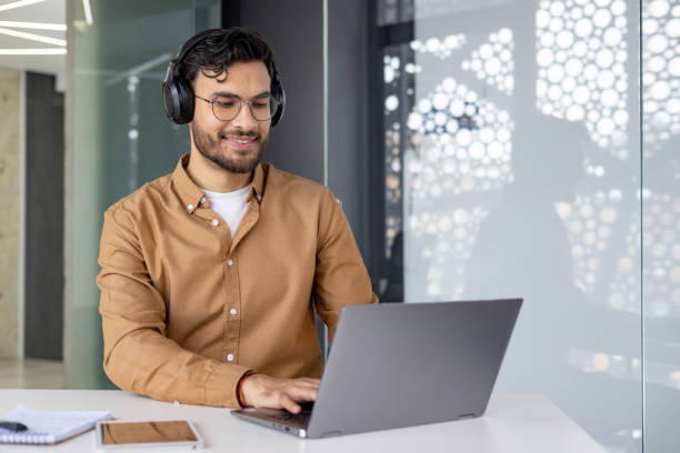 istock Smiling man with headphones working on a laptop in a modern office 2156267810