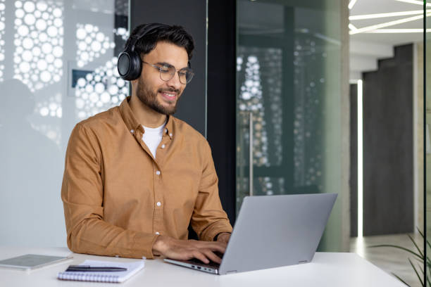 istock Smiling man in headphones working on laptop in modern office 2156268769