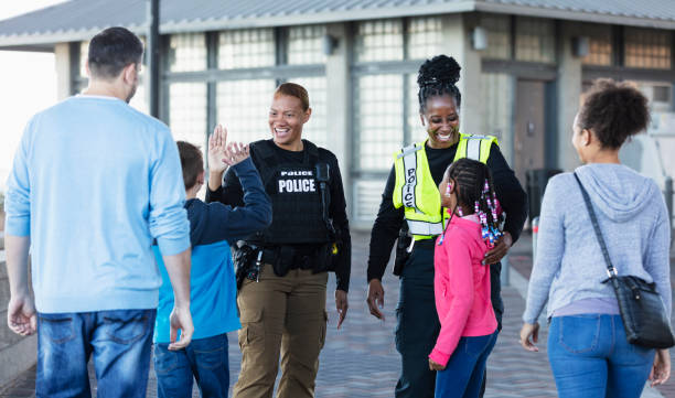 Two policewomen greeting community members Two multiracial policewomen, in their 40s and 50s, conversing outdoors with two children and their parents. The view is from over the shoulders of the families, and the focus is on the police officers who are smiling at the children. One is giving a high five to the 11 year old boy. female police officer stock pictures, royalty-free photos & images